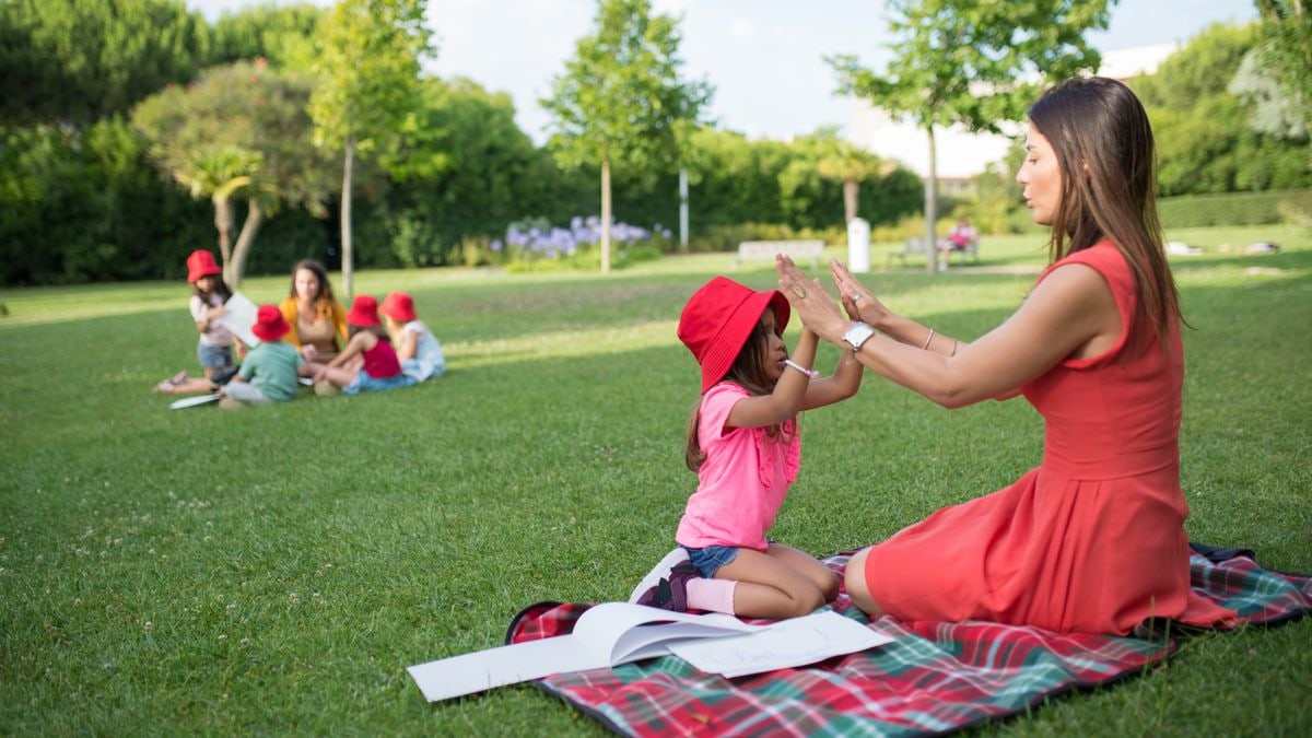 Joyful interaction between a child and woman in a sunny park, surrounded by nature and other children.